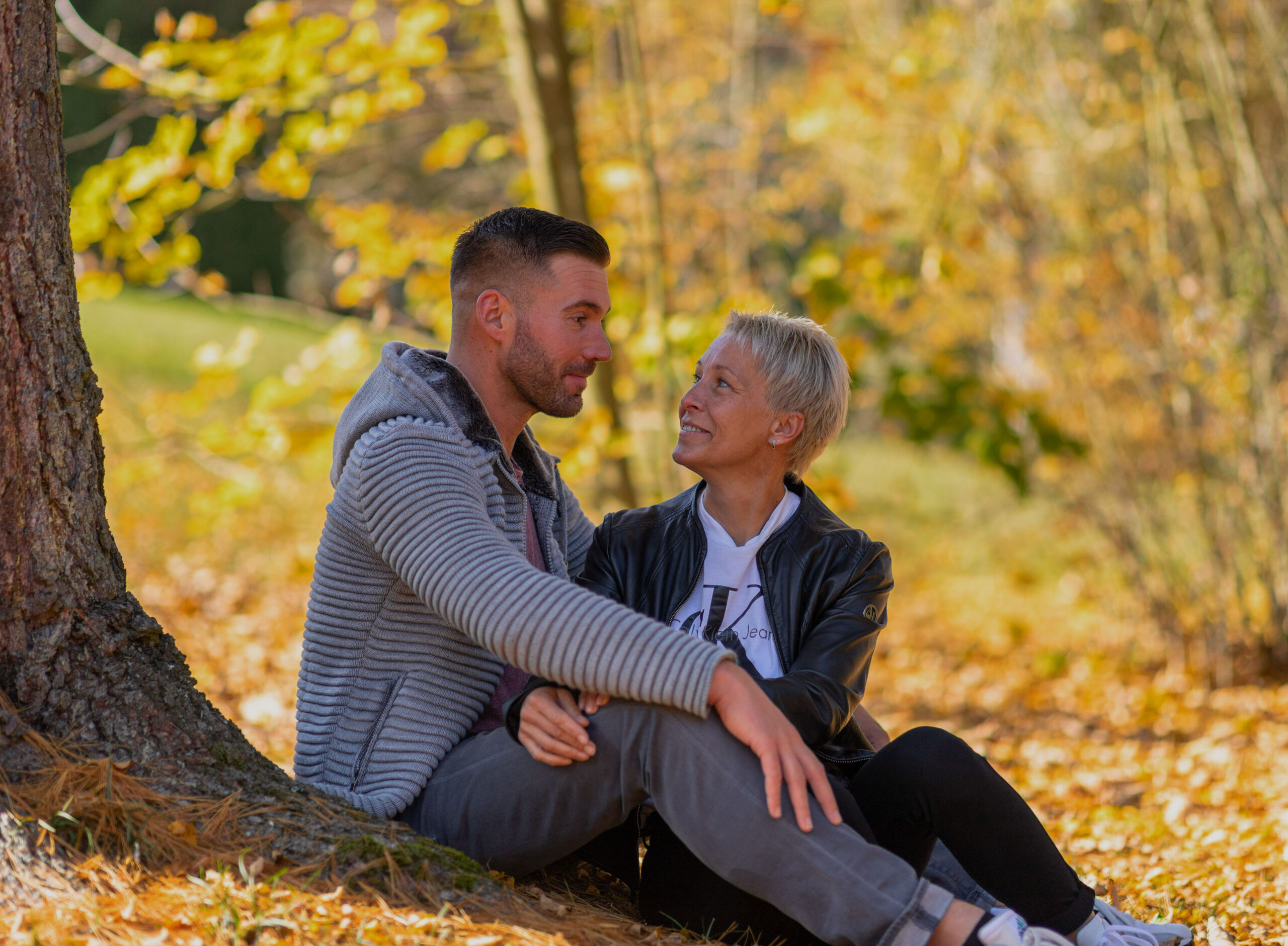 Pärchen sitzt unter einem Baum im Herbstlaub, Portraitfotografie, Portraits im Erzgebirge, Fotoshooting Erzgebirge, Fotoshooting in Thermalbad-Wiesenbad, Portraitshooting Annaberg-Buchholz und Umgebung