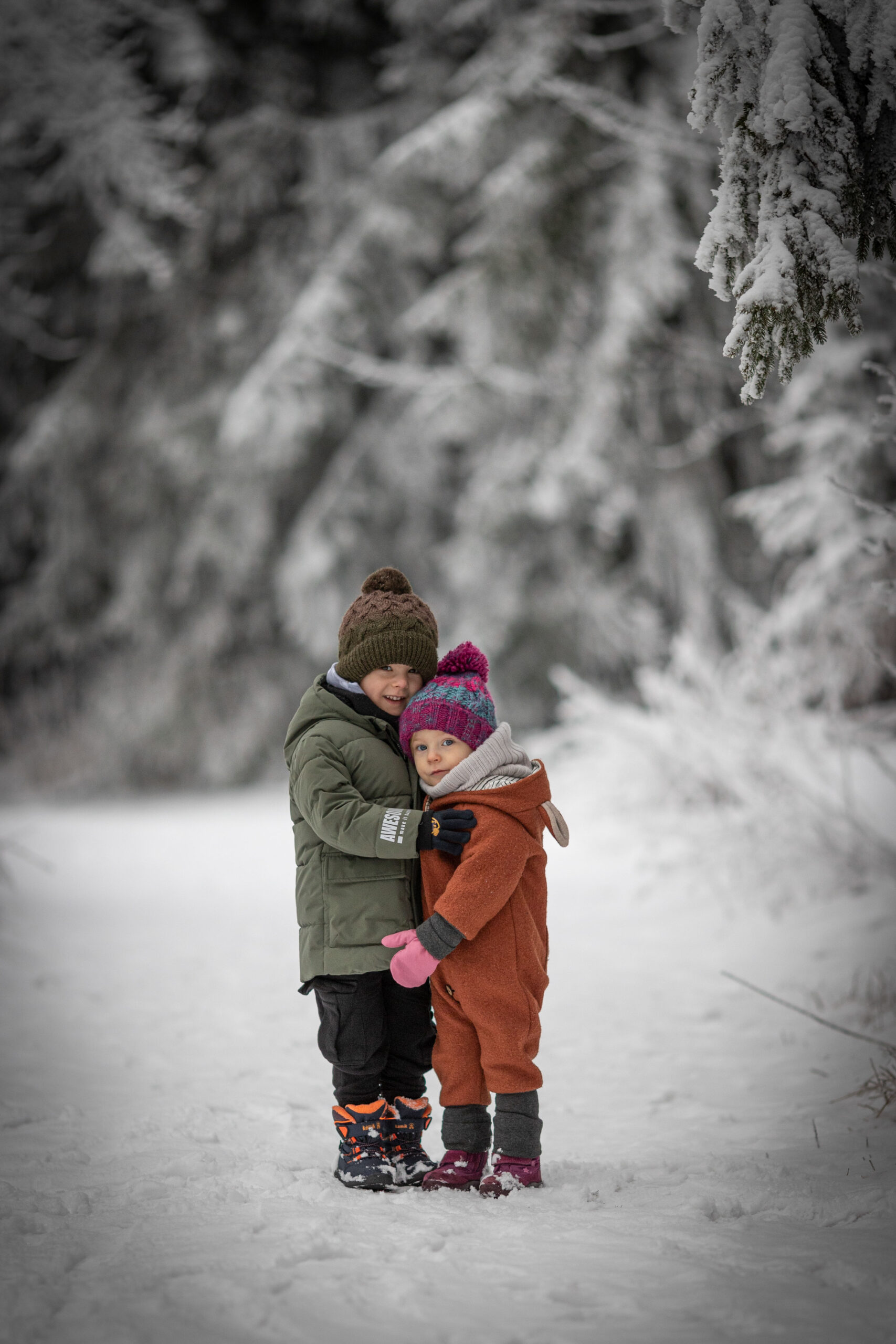 Zwei Kleinkinder stehen aneinandergelehnt im Winterwald des Erzgebirges