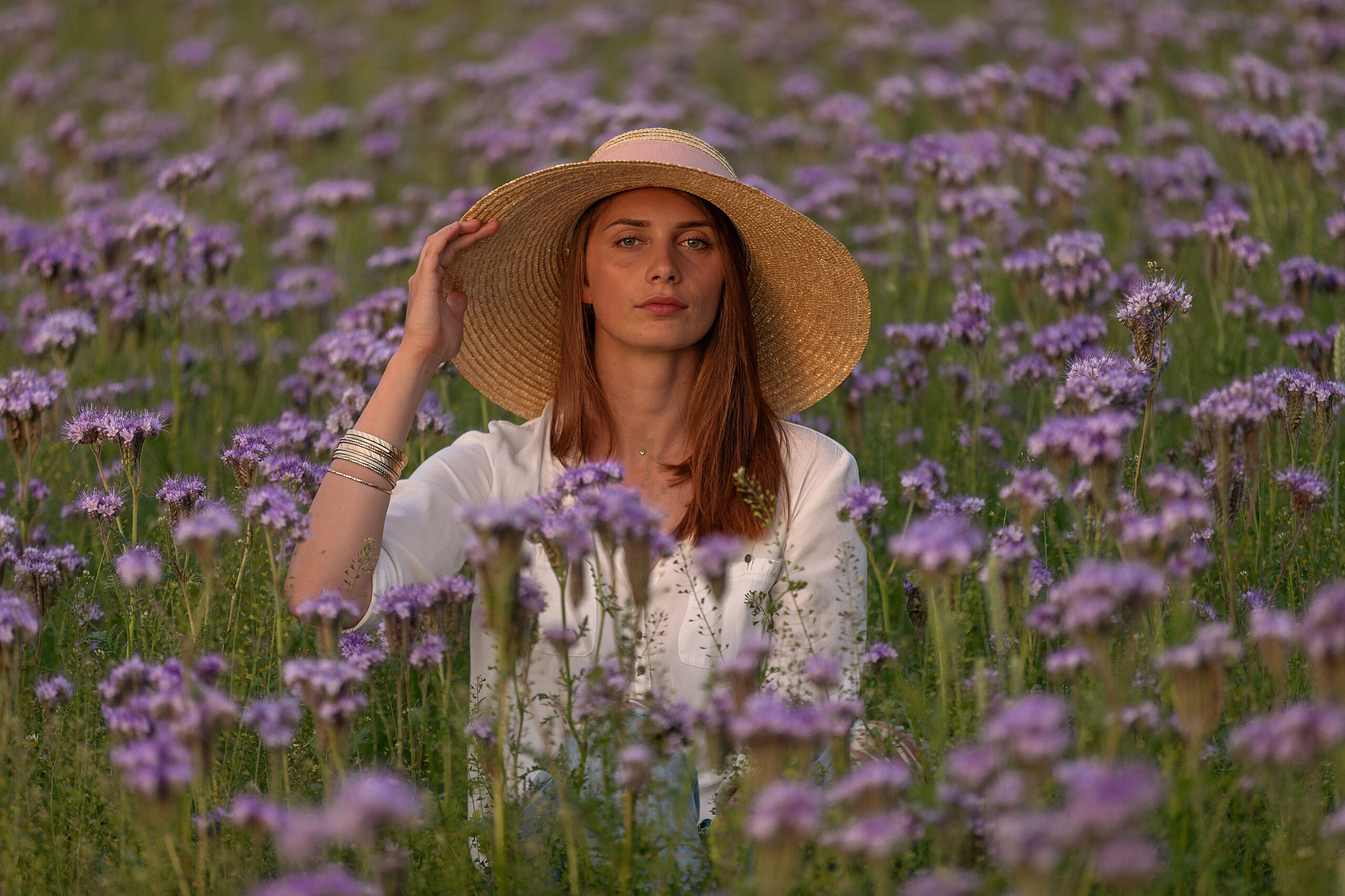 Junge Frau mit großem Sonnenhut sitzt in einem Feld mit lila Blumen