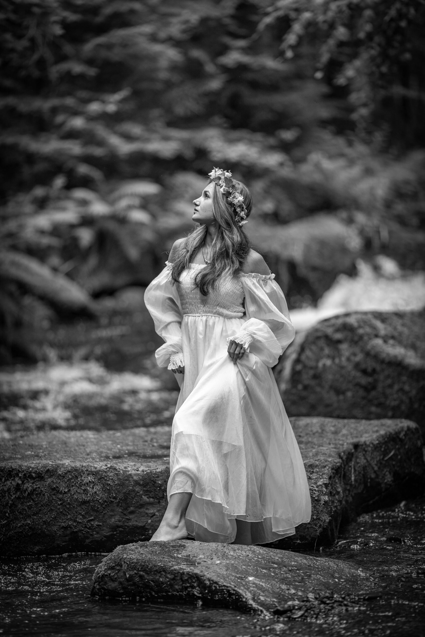 Porträt einer jungen Frau in weißem Kleid mit Blumenkranz im Haar steht auf einem Stein eines Baches im Erzgebirge
