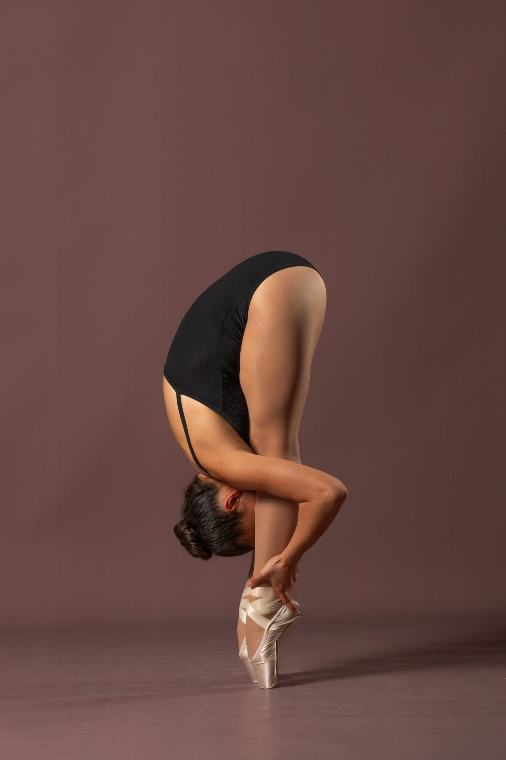 Ballerina beugt sich tief so das ihr Kopf zwischen den Schienbeinen steckt