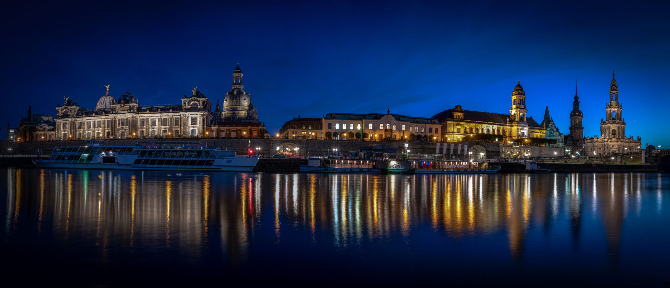 Panorama der Skyline von Dresden zur blauen Stunde, im Vordergrund die Elbe