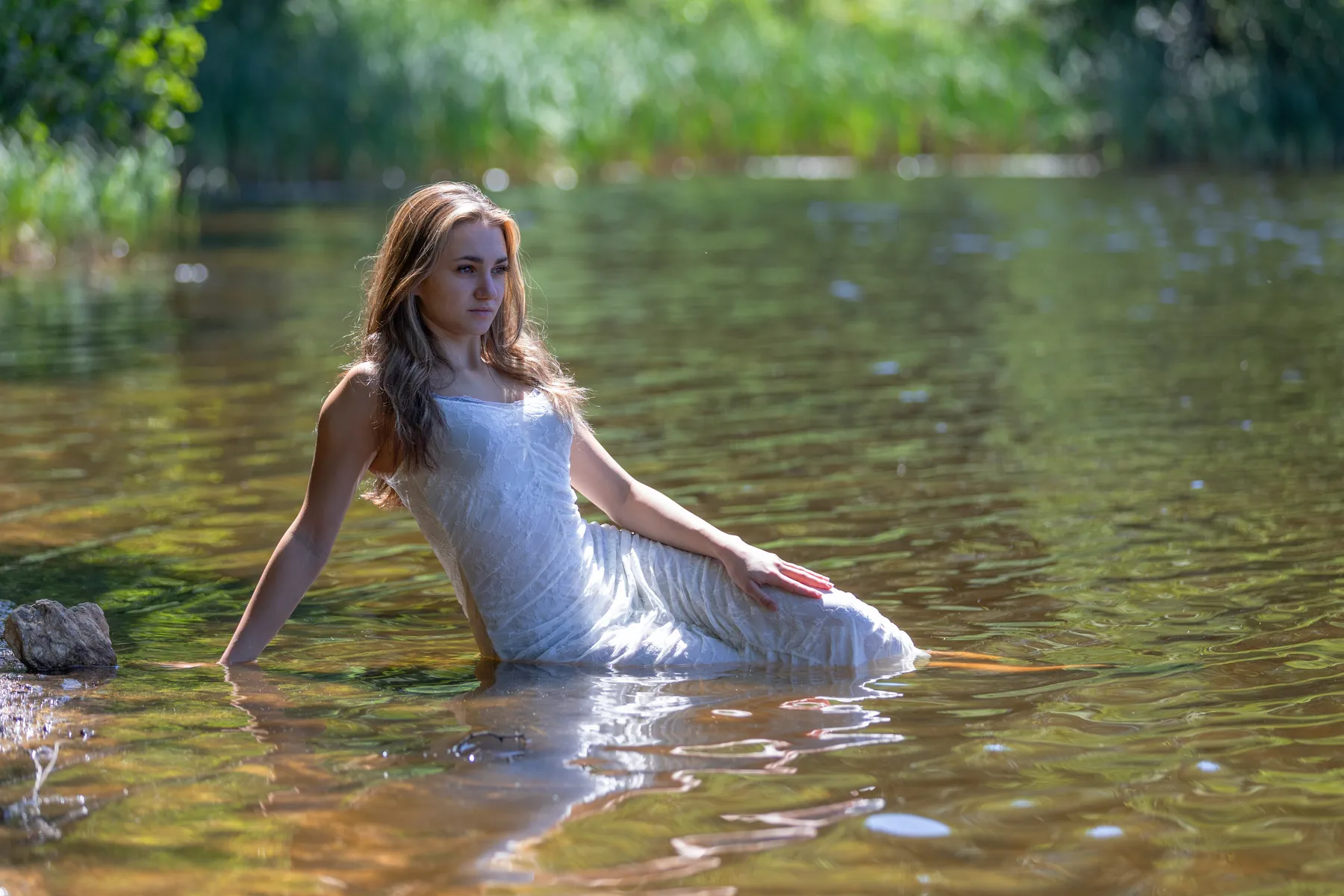Portraitfoto junge Frau sitzt im Wasser am Ufer des Schwarzen Teiches bei Elterlein, sie ist mit einem langen weißen Kleid bekleidet