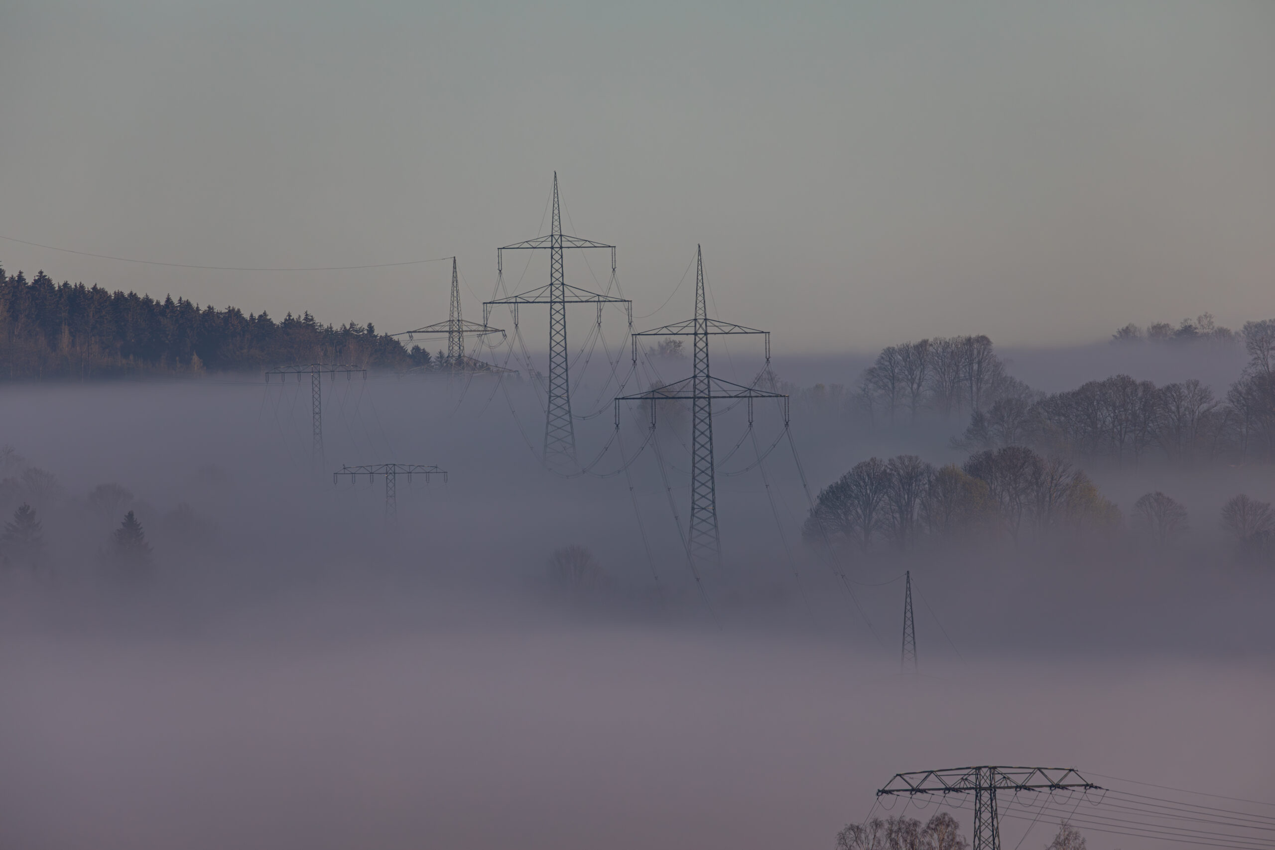 Strommasten ragen aus dichtem Hochnebel über einer Landschaft