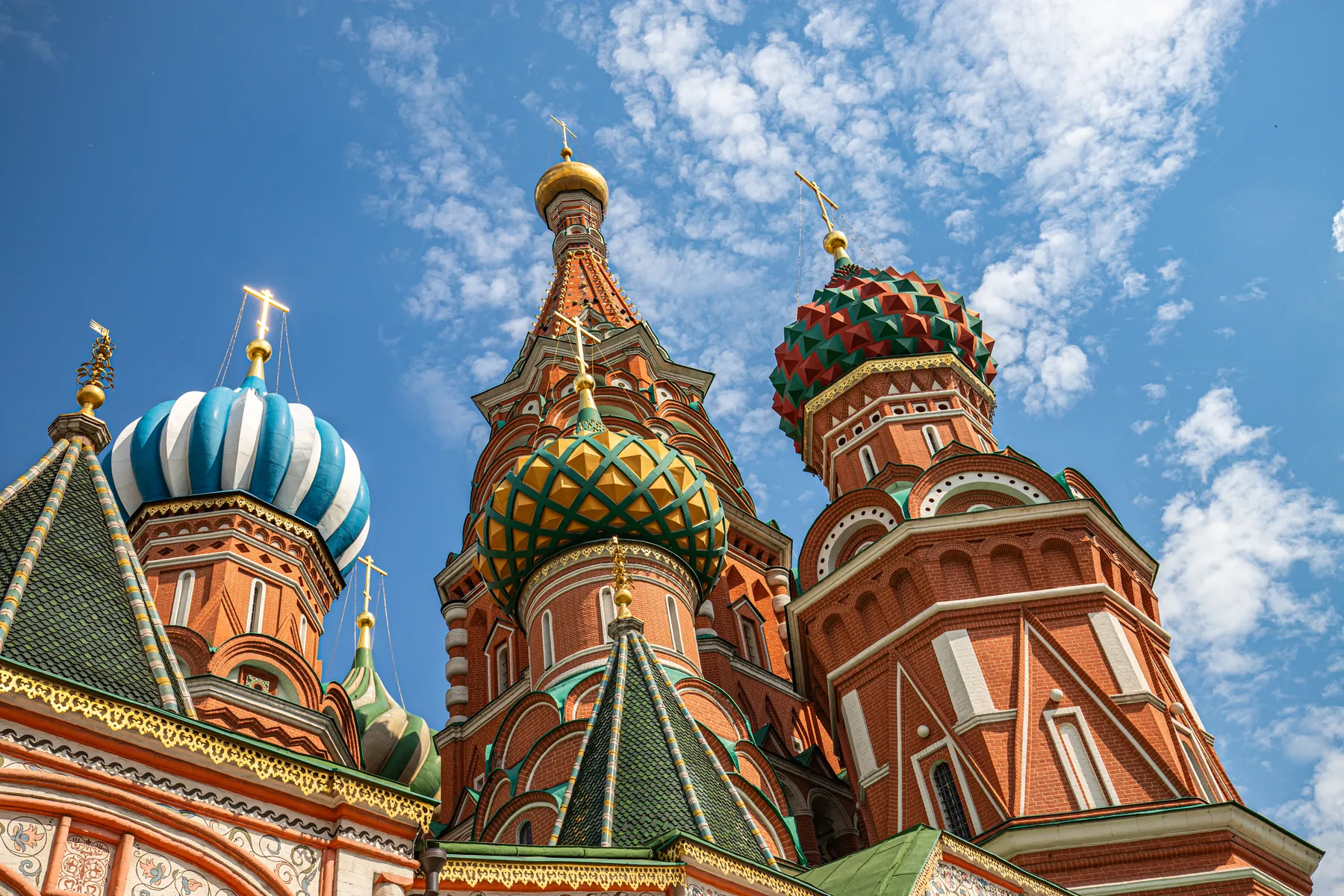 Landschaftsfotografie der farbenfrohen zwiebelförmigen Kuppeln und verschnörkelten Türme der Basilius-Kathedrale in Moskau, Russland, stehen vor einem strahlend blauen Himmel mit vereinzelten Wolken und zeigen komplizierte Muster und lebhafte Details.