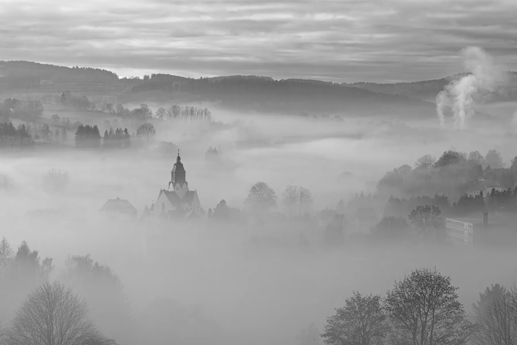 Kirche von Wiesa im Erzgebirge ragt aus dichtem Morgennebel in einer ruhigen Tallandschaft