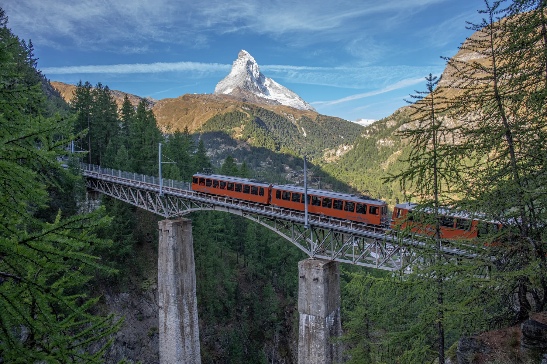 Die Gornergratbahn überquert die Findelbachbrücke welche über eine hohe Schlucht führt. Die Brücke ist umgeben von Lärchenwald und im Hintergrund erhebt sich das Matterhorn