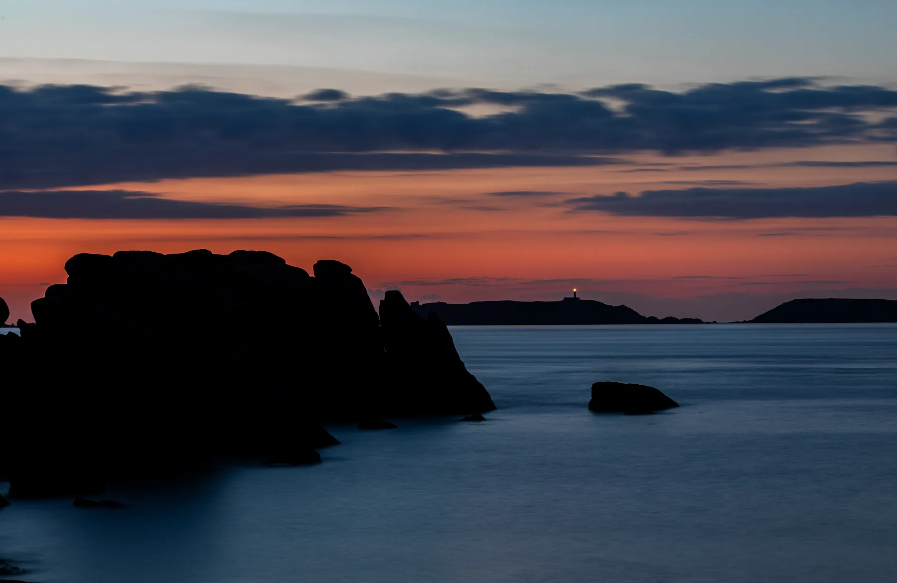 Landschaftsfotografie einer felsigen Küstenlandschaft der Bretagne bei dramatischem Sonnenuntergang der den Horizont in tiefes rot taucht