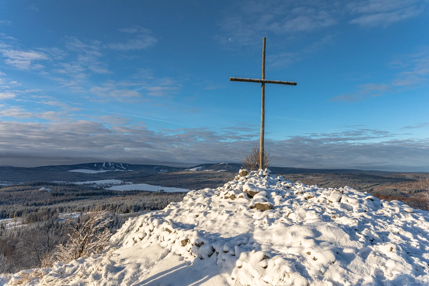Gipfelkreuz auf dem verschneiten Gipfel des Spičak mit weiter Aussicht über das Erzgebirge