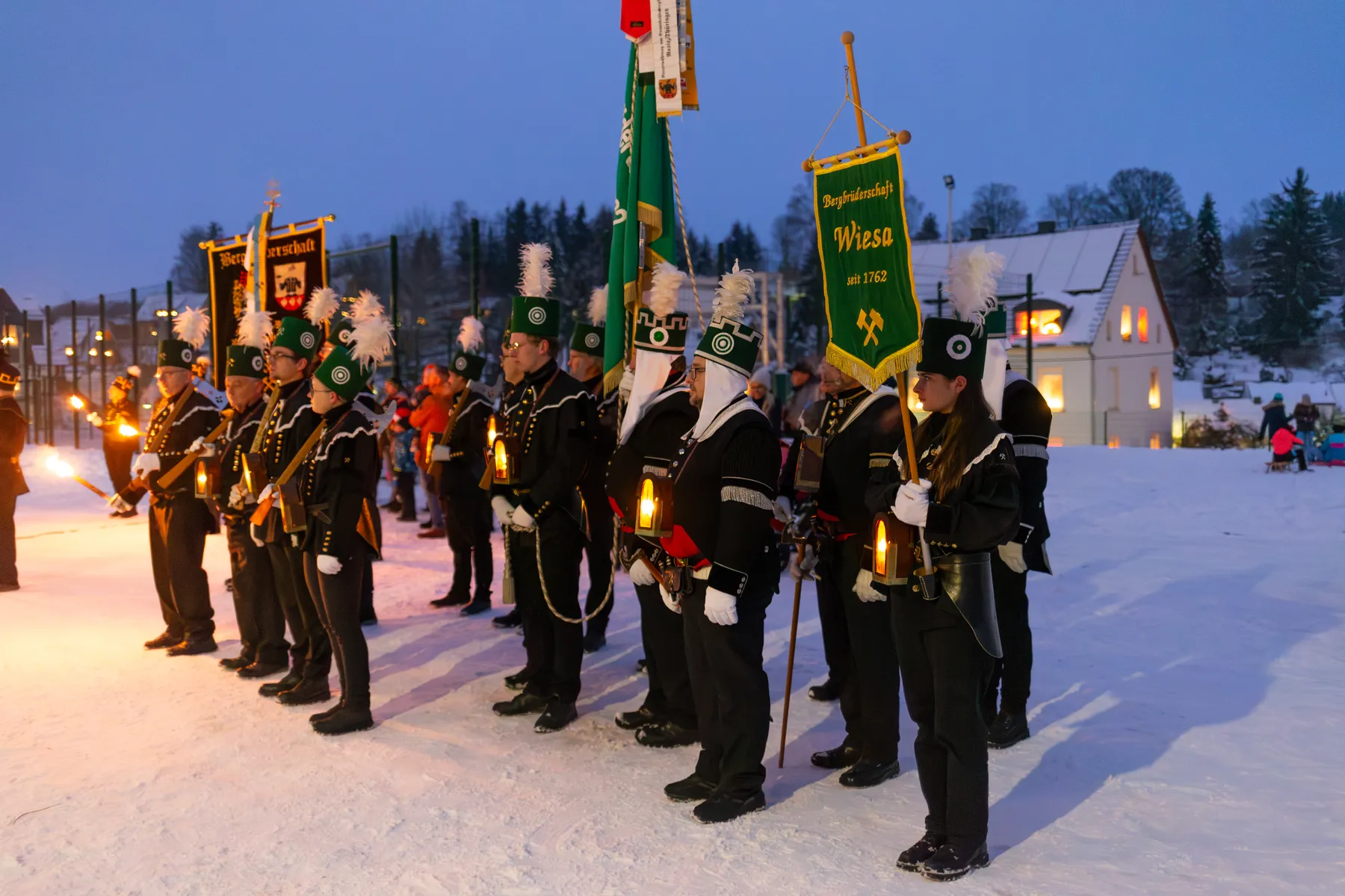 Bergbrüderschaft Wiesa mit historischen Uniformen und Fahnen bei winterlicher Abendstimmung
