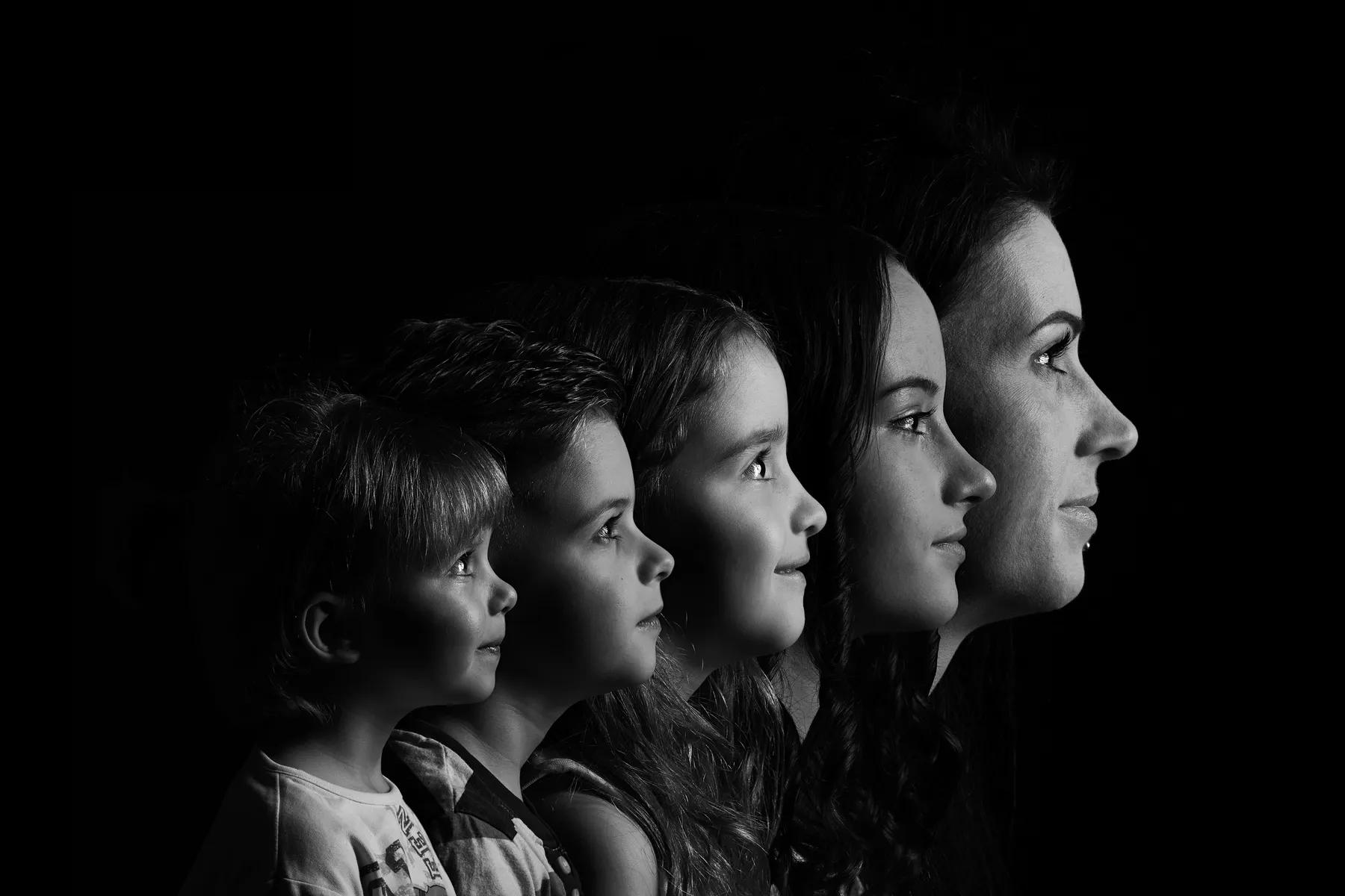 Schwarz-weiße Portraitfotografie mit mehreren Profilansichten eines weiblichen Gesichts von Kindheit bis Erwachsenenalter vor dunklem Hintergrund.