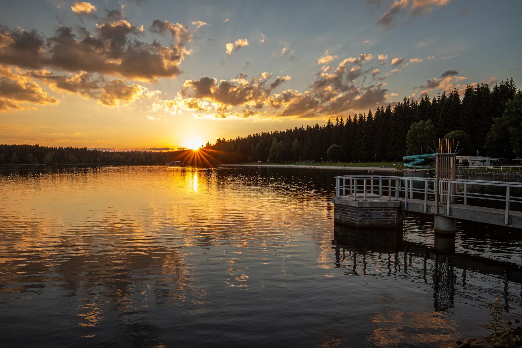 Steg am Geyrischen Teich bei Sonnenuntergang mit Spiegelungen im ruhigen Wasser