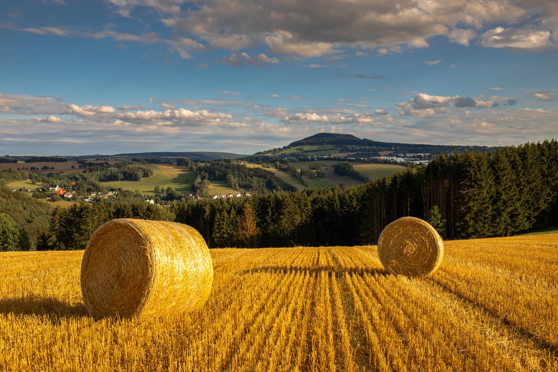 Ein abgeerntetes Kornfeld im Erzgebirge auf dem Strohballen liegen und im Hintergrund der Pöhlberg zu sehen ist