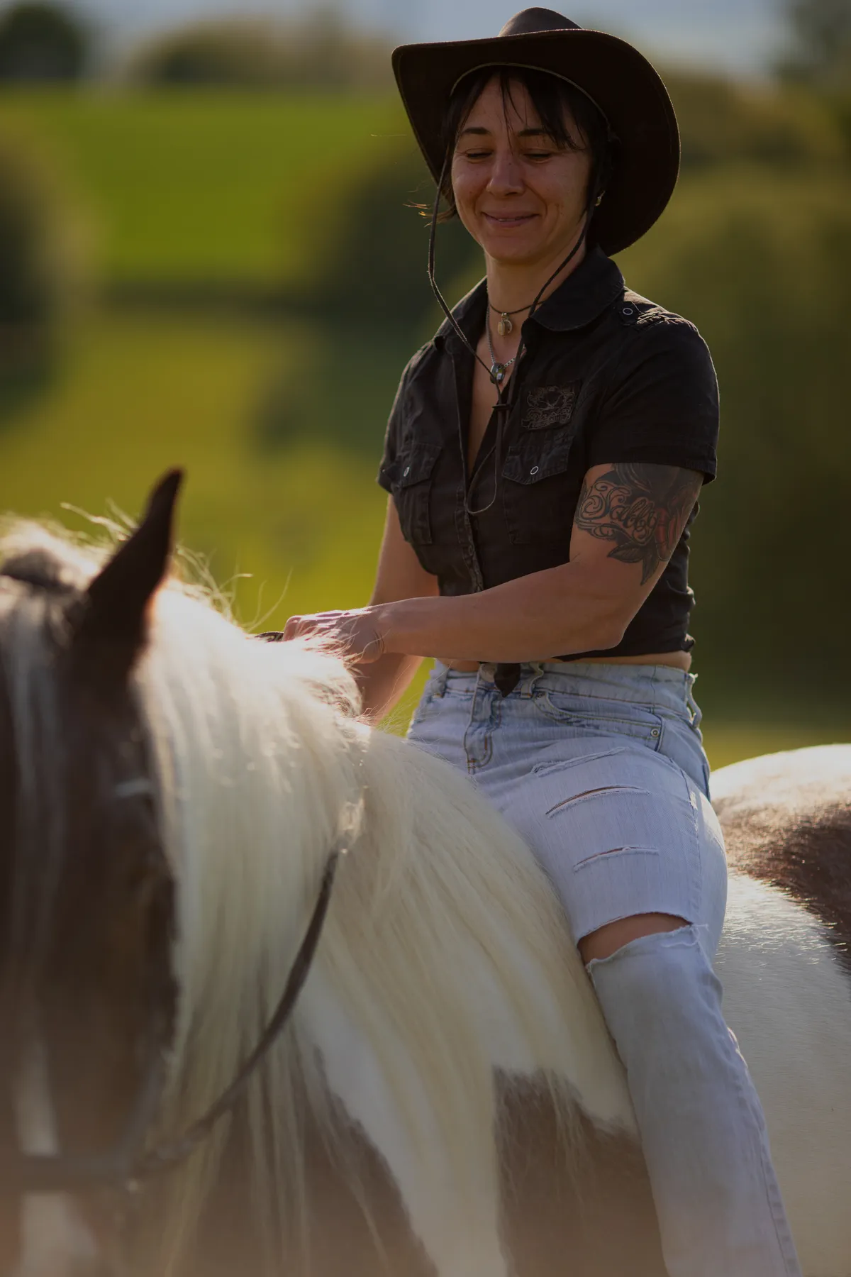 Frau in Jeans und Hemd mit Cowboyhut reitet auf geschecktem Pferd