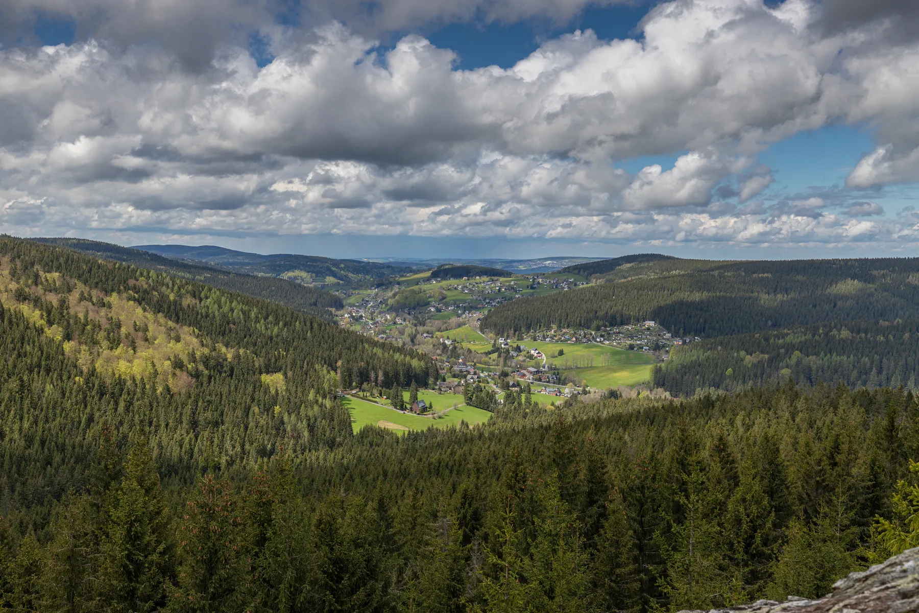 Blick vom Taubenfelsen über ein weites Erzgebirgstal mit Wäldern, Wiesen und der Ortschaft Rittersgrün unter dramatischem Wolkenhimmel