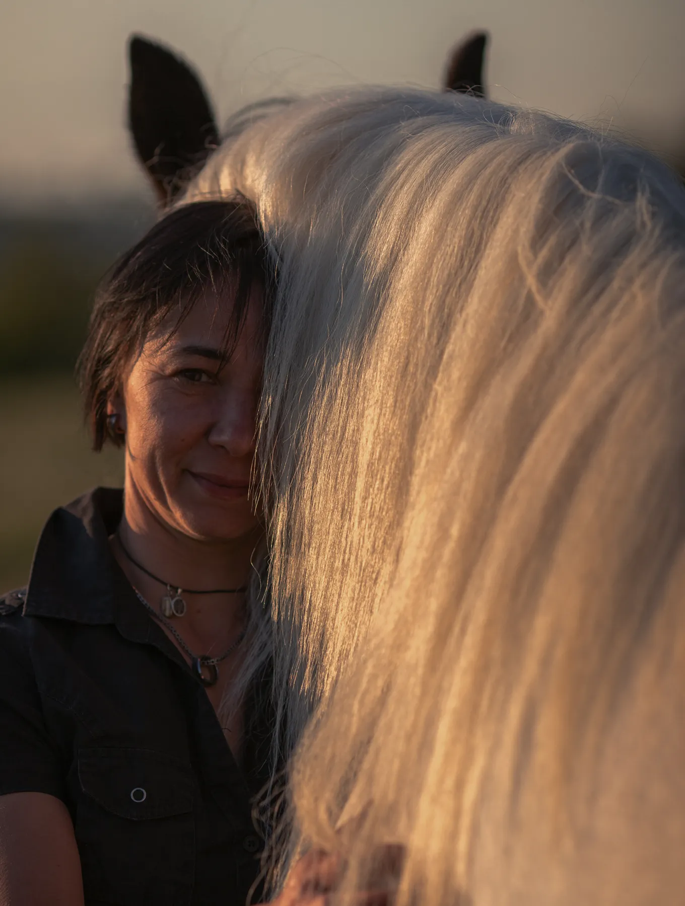 Emotionale Pferdefotografie bei goldenem Abendlicht: Eine Frau steht innig an der Seite eines weißen Pferdes, dessen Mähne das Bild weich umrahmt. Die ruhige Stimmung, Nähe und Vertrauen zwischen Mensch und Tier machen diese Pferdefotografie zu einem authentischen, natürlichen Moment in der Natur.