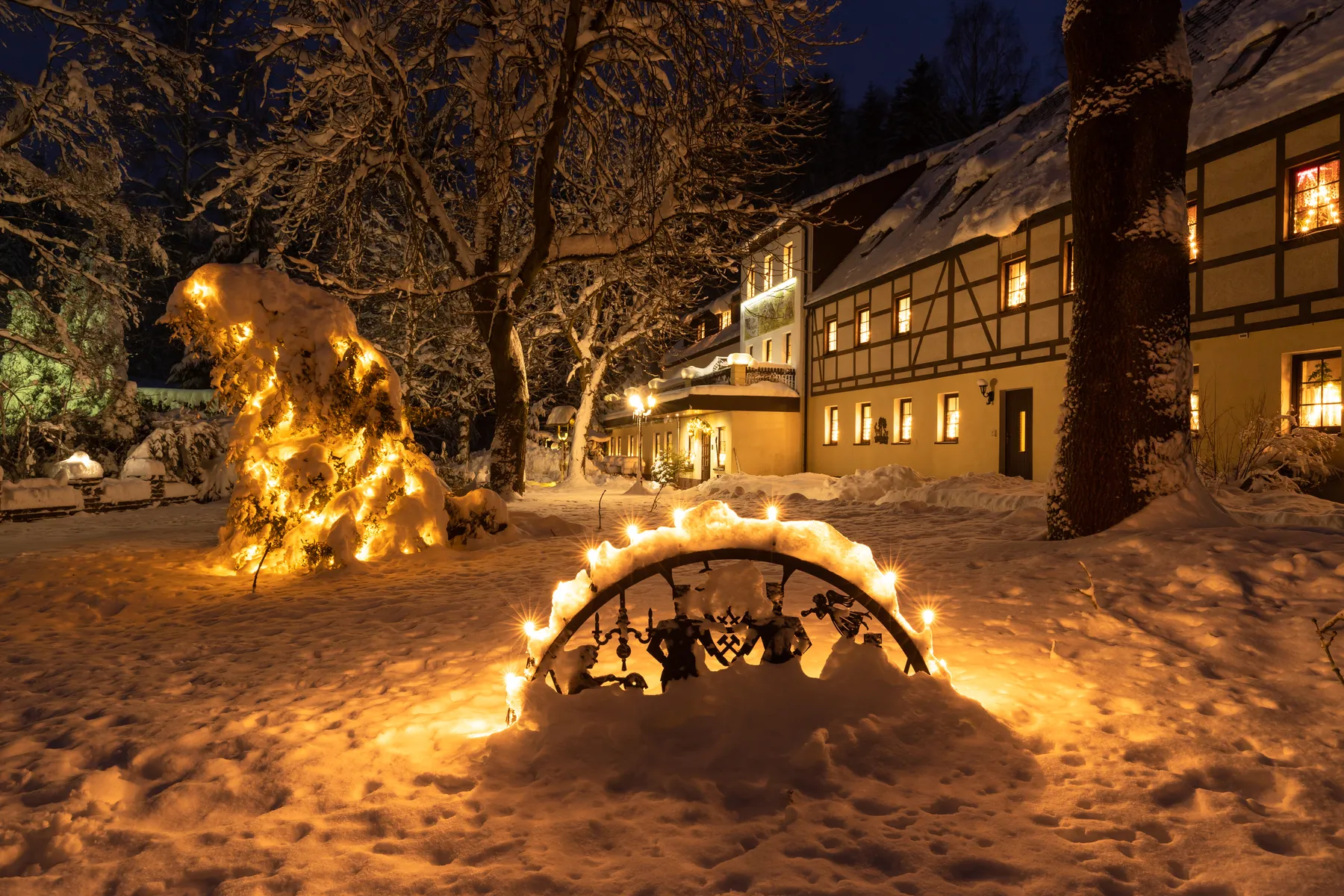 Verschneiter Hof des Hotels und Gasthofes Sauwald in Tannenberg mit warm beleuchteten Fenstern und Bäumen in nächtlicher Winterstimmung