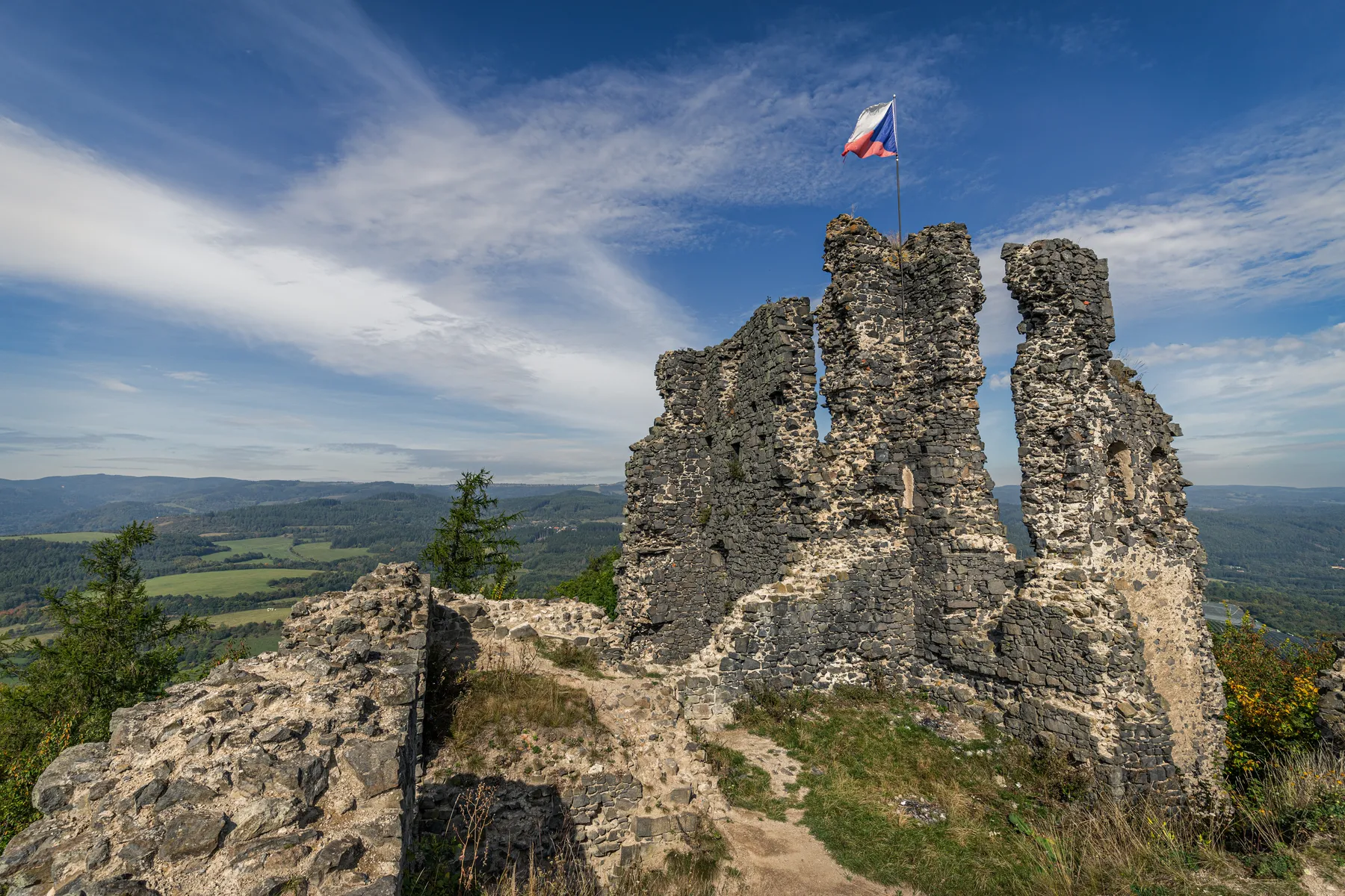 Burgruine Šumburk auf felsigem Höhenzug im Böhmischen Erzgebirge mit Fahne und weitem Blick über die umliegende Landschaft