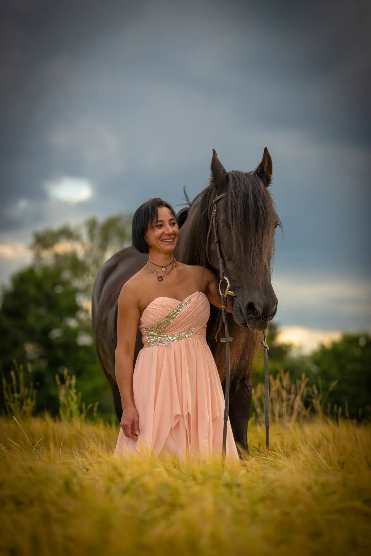 Junge Frau in rosa Kleid steht mit ihrem Pferd in unreifem Getreidefeld