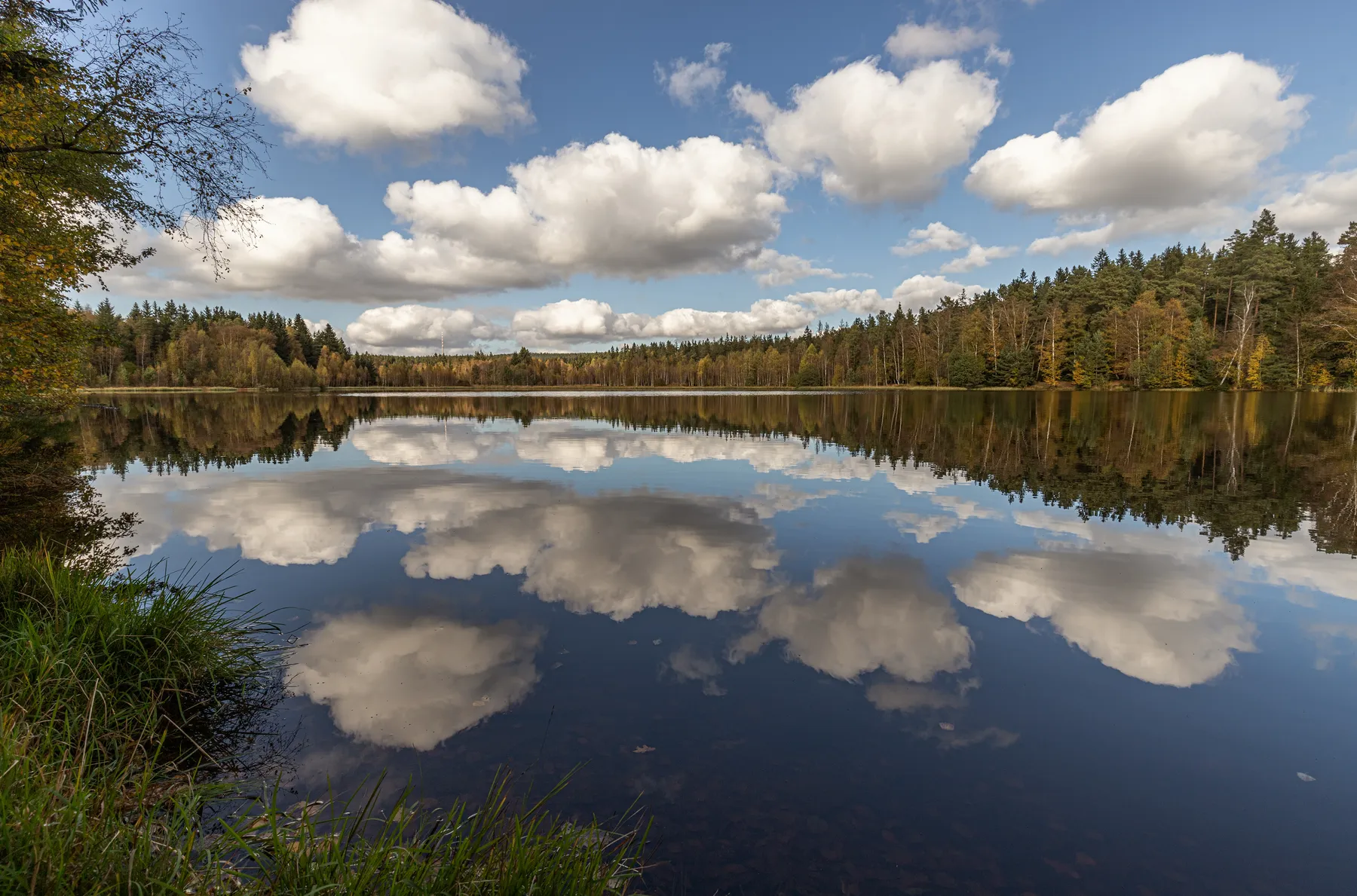 Schwarzer Teich bei Elterlein mit spiegelnden Wolken und herbstlich gefärbtem Baumbestand