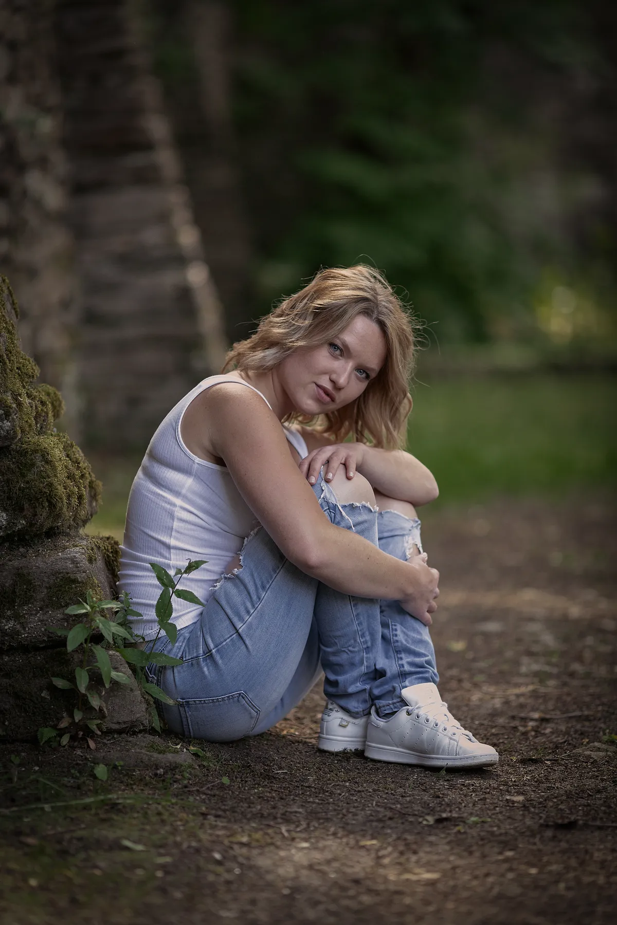 Outdoor-Portrait einer jungen Frau, sitzend an einer moosbewachsenen Steinmauer im Wald, fotografiert bei natürlichem Licht im Erzgebirge.