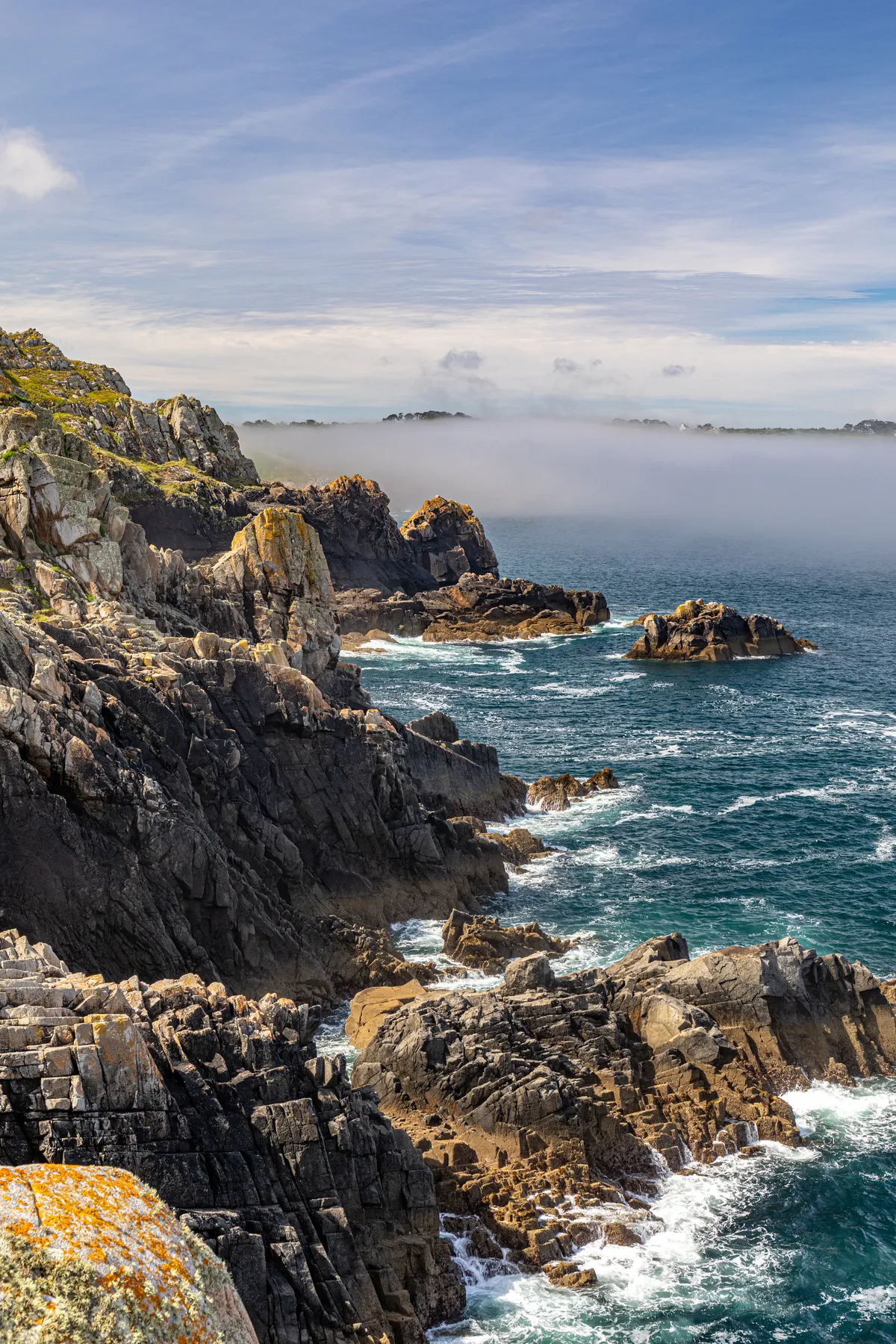Landschaftsfotografie einer schroffen Küste in der Bretagne an deren Felsen Meereswellen schlagen