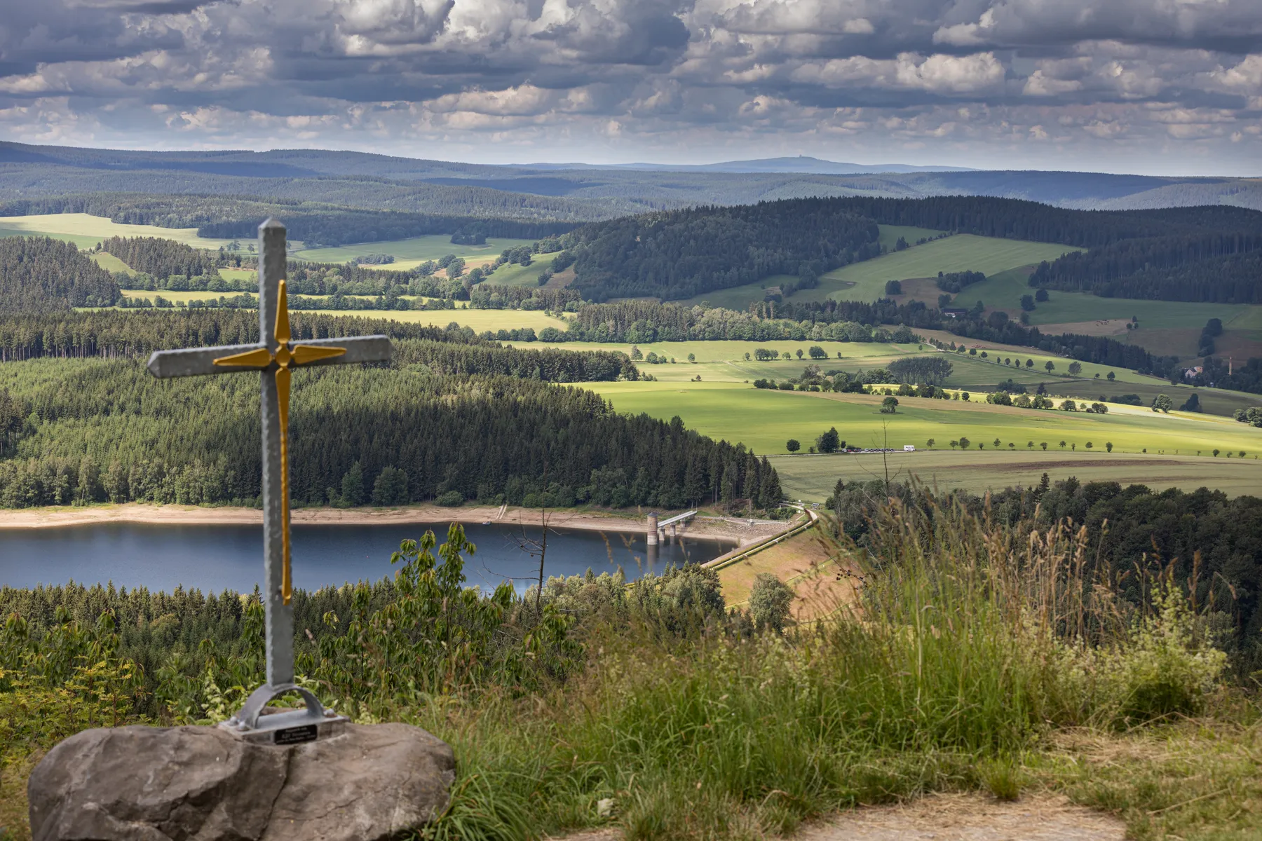 Aussicht vom Bärenstein mit Kreuz im Vordergrund und Blick auf Stausee, Wälder und Felder in weiter Landschaft