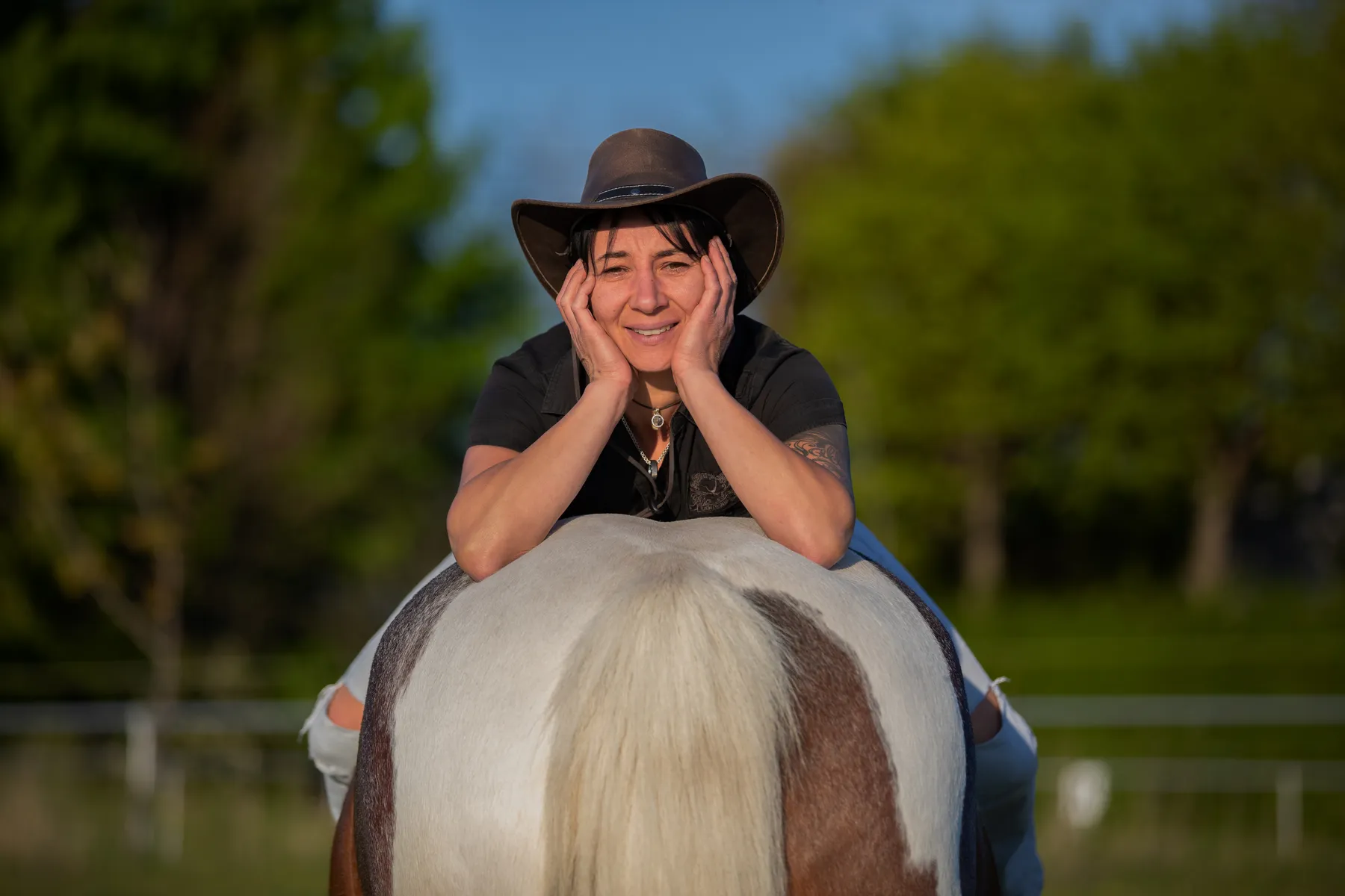 Eine Frau mit Cowboyhut sitzt auf ihrem Pferd verkehrt herum und stützt ihr Gesicht in ihre Hände