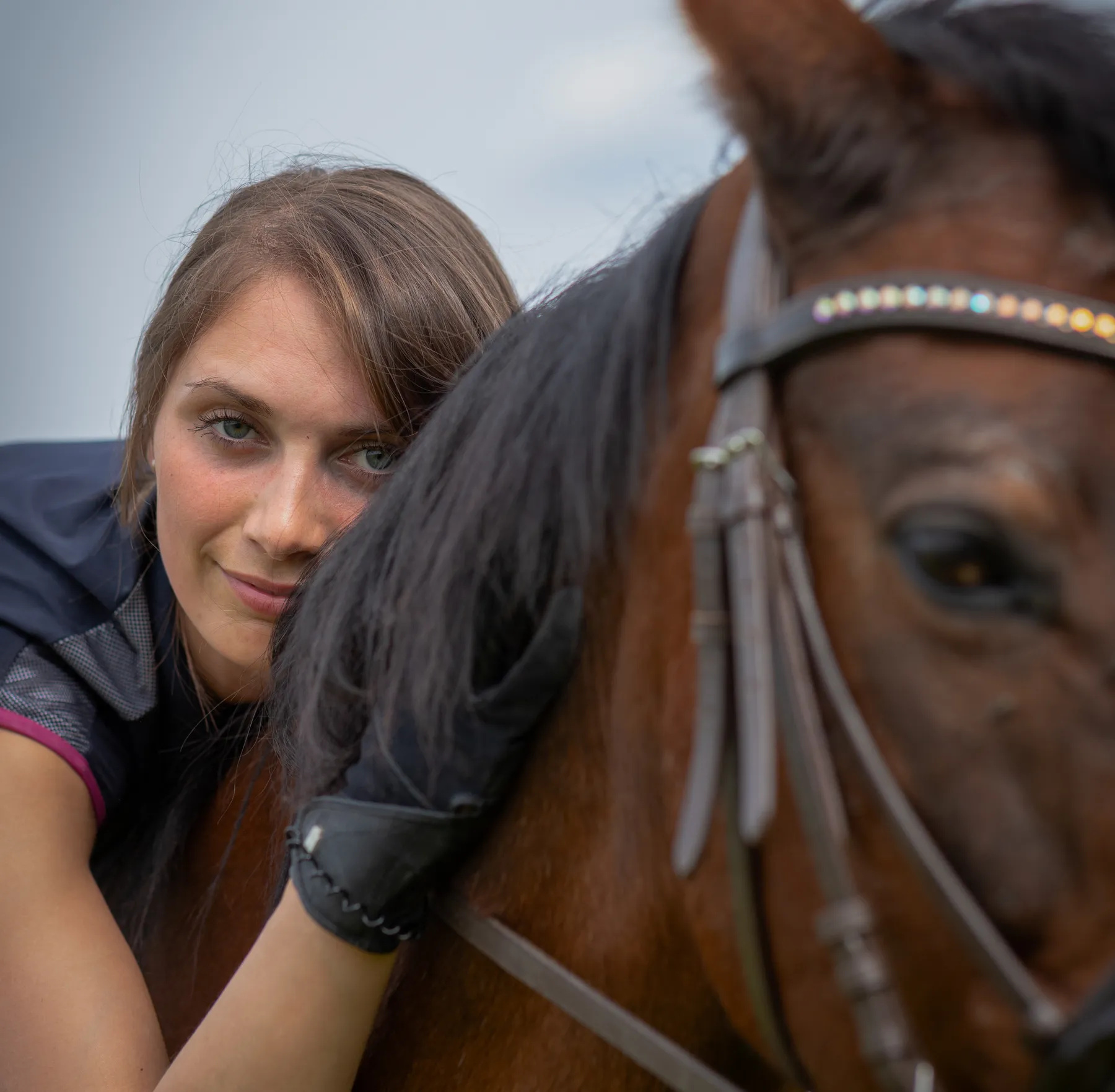 Eine junge Frau liegt auf ihrem Pferd und hat ihr en Kopf auf seinen Hals gelegt, vom Pferdekopf ist nur ein Teil zu sehen