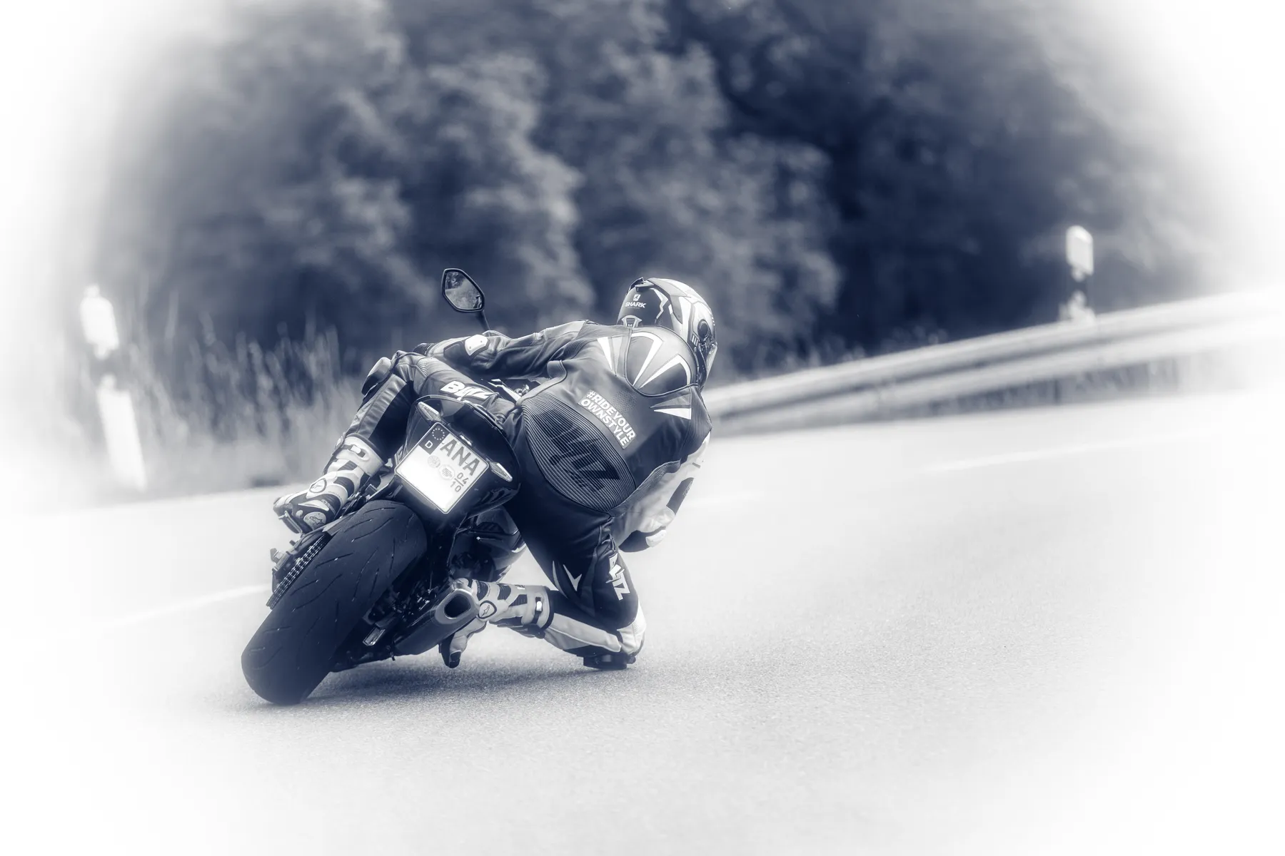 Motorradfahrer fährt in Schräglage in eine Kurve und setzt sein Knie auf den Asphalt. Das Foto ist schwarz weiß mit starker Vignette.
