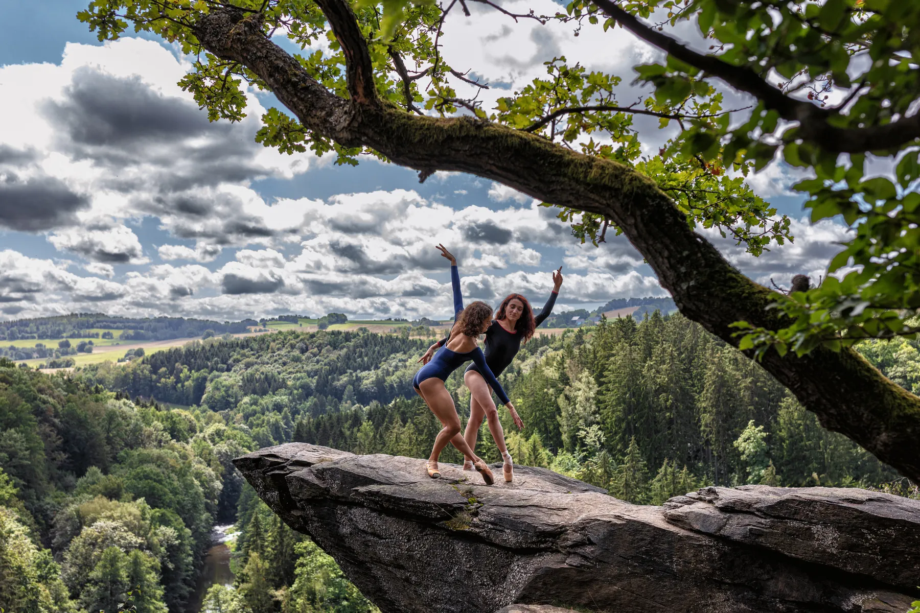 Zwei Balletttänzerinnen auf einem Felsen über der bewaldeten Landschaft des Erzgebirges