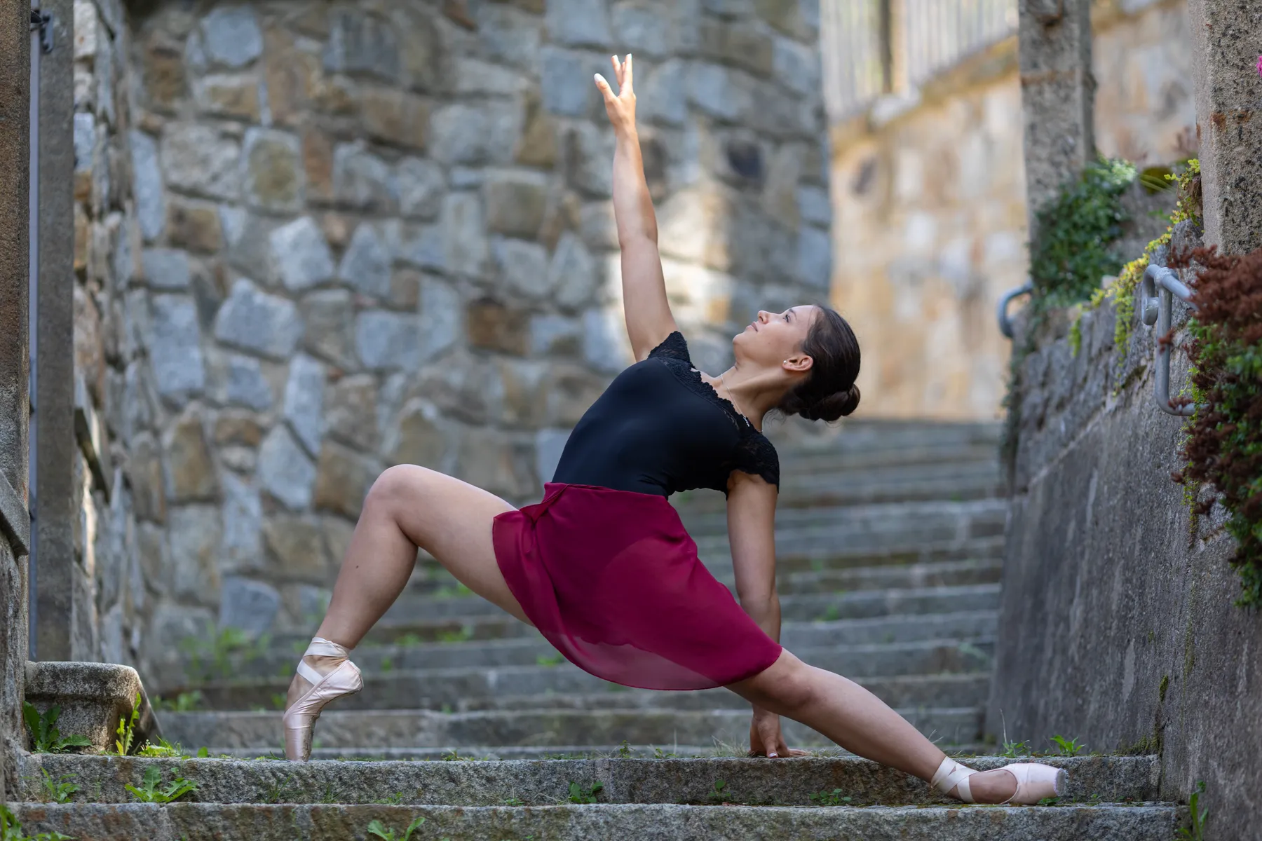Auf einer Steintreppe umgeben von Steinmauern steht eine Ballerina und macht eine Pose